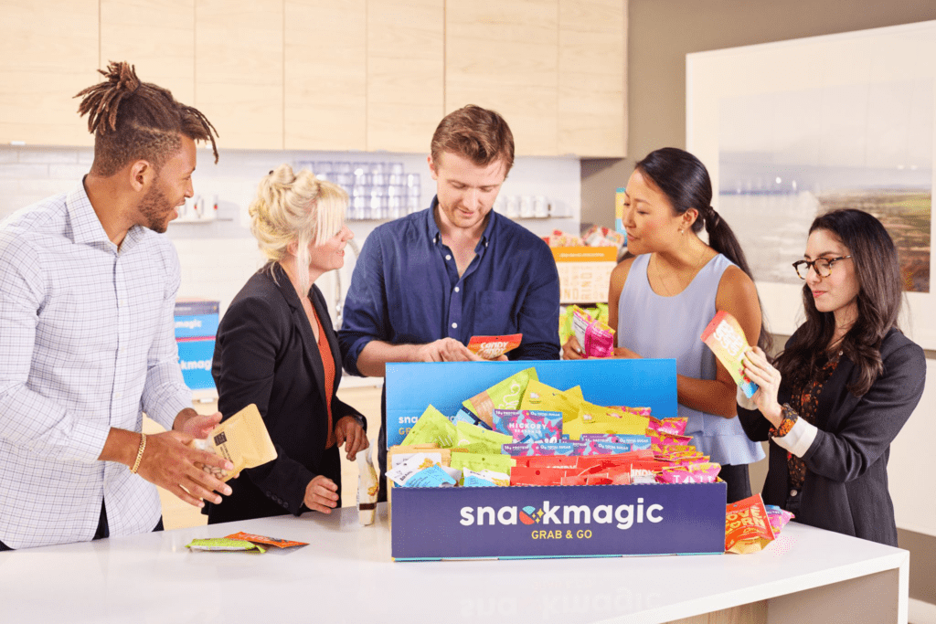 Coworkers gather around a table with a snack box in the middle