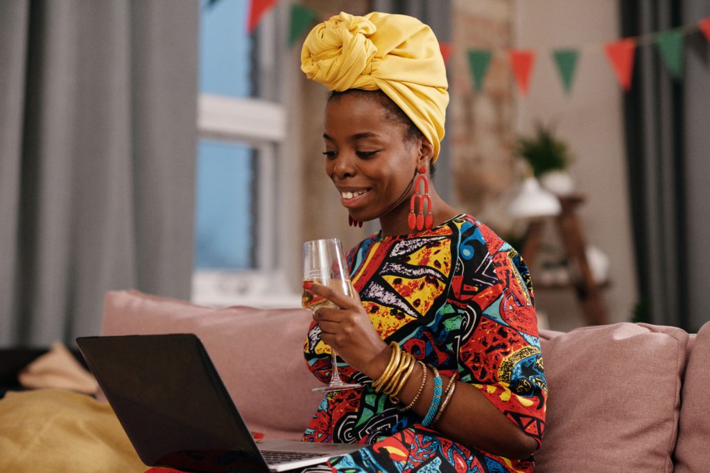 woman enjoying a glass of wine while attending a meeting on her laptop
