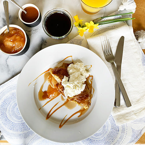 A bright breakfast spread with french toast as the main dish. Coffee, juice, and syrups surround the plate with daffodils nearby as decoration.
