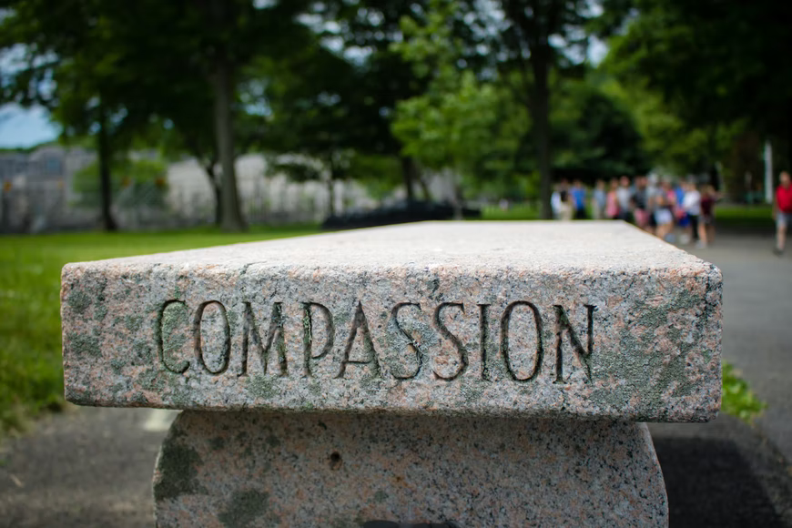 An outdoor stone bench with the word "Compassion" engraved on its side.