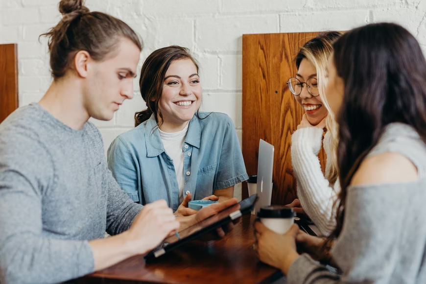 Four young coworkers share a laugh and a coffee at work.