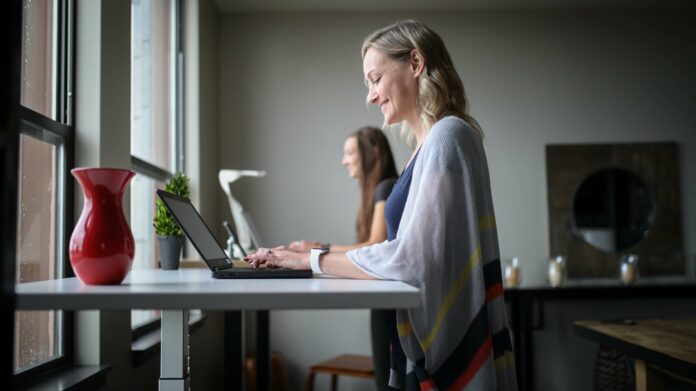 A woman smiling on her laptop at her standing desk.