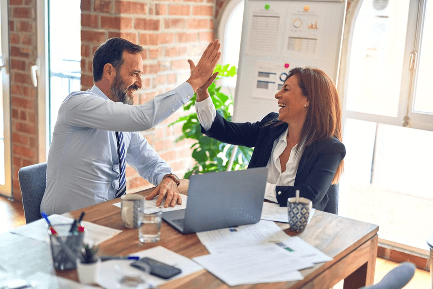 Two coworkers celebrating and high-fiving at work.