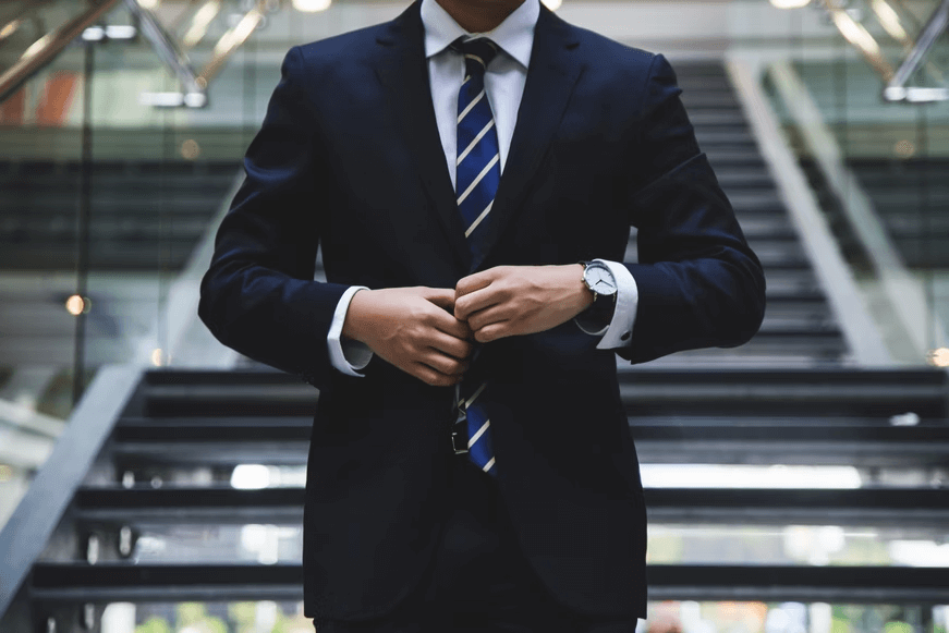 A professional buttoning up his suit in front of a flight of stairs.