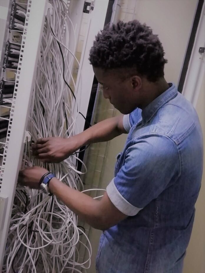 A young man working in a server room with lots of wires.